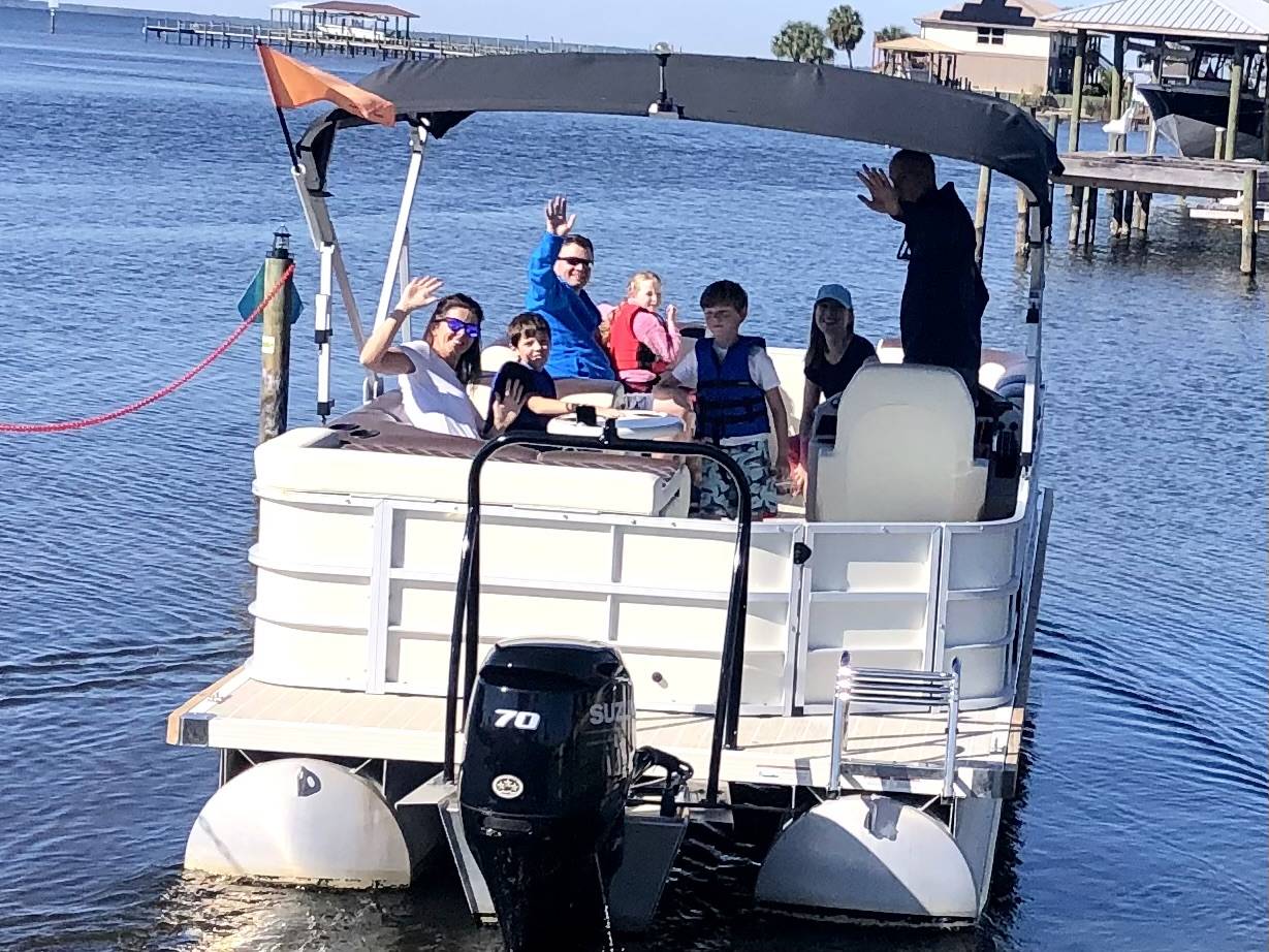 Family waving from a Panama City pontoon rental, enjoying a day on the water.