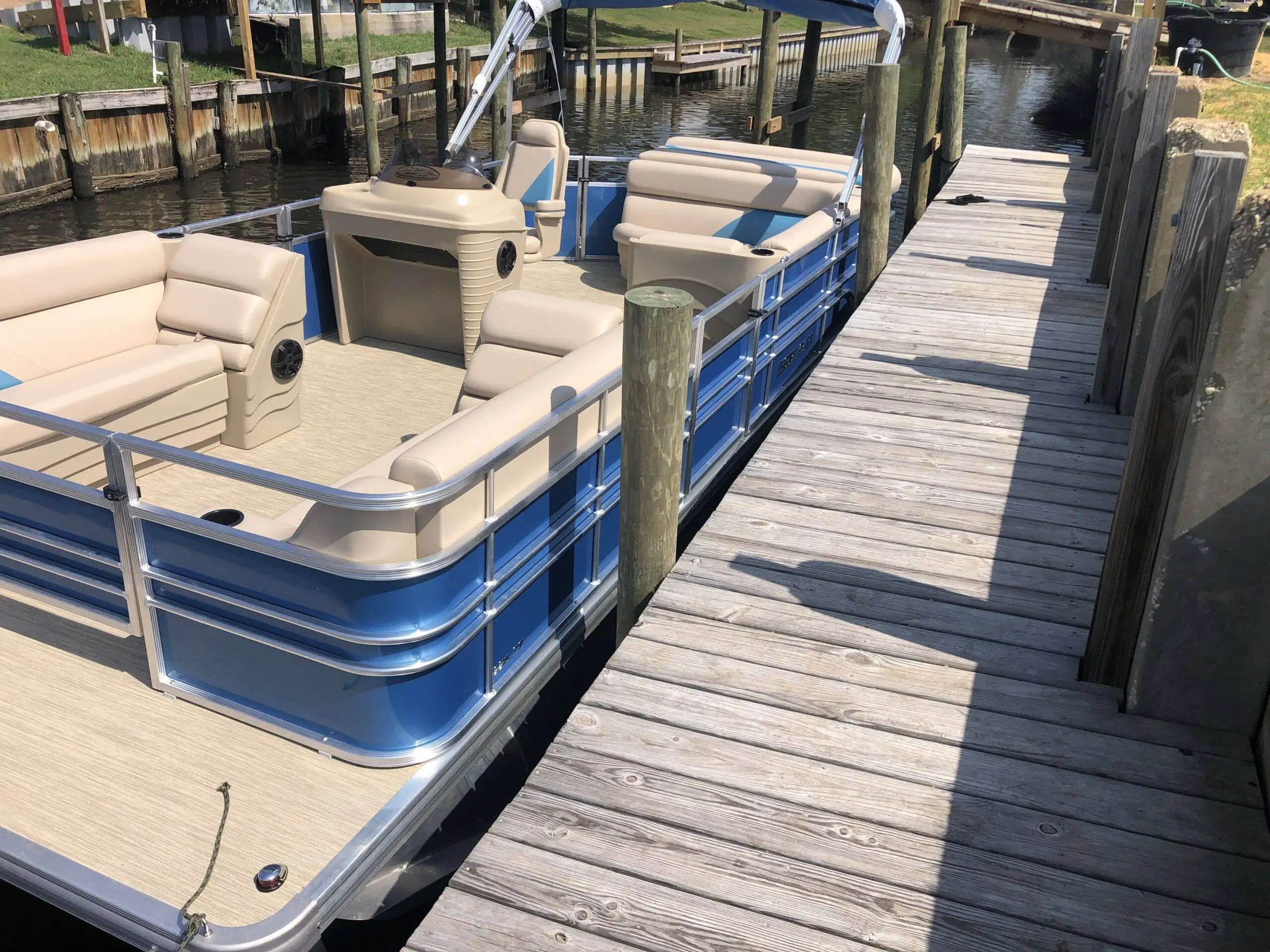 A spacious blue and beige pontoon boat moored at a wooden dock, ready for renting in Panama City.