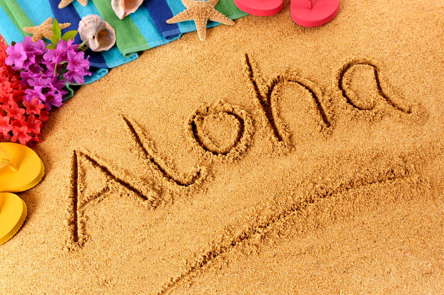 "Aloha" written in sand with flowers and flip-flops, from Ultimate Pontoon Guide.