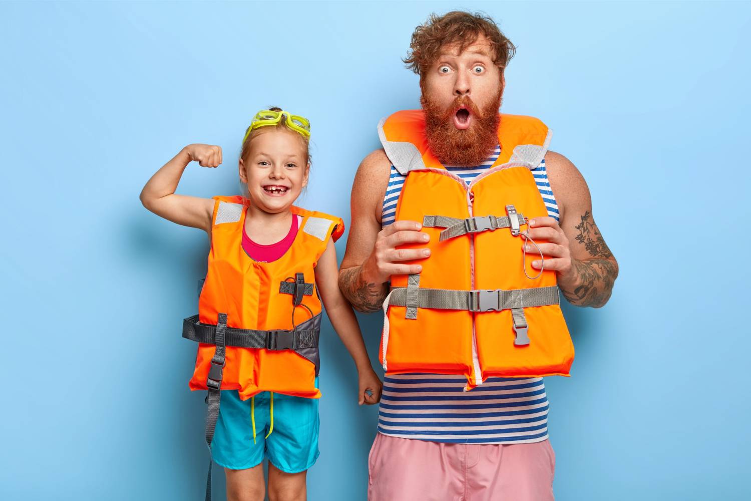 A surprised bearded man and a smiling girl wearing life jackets.