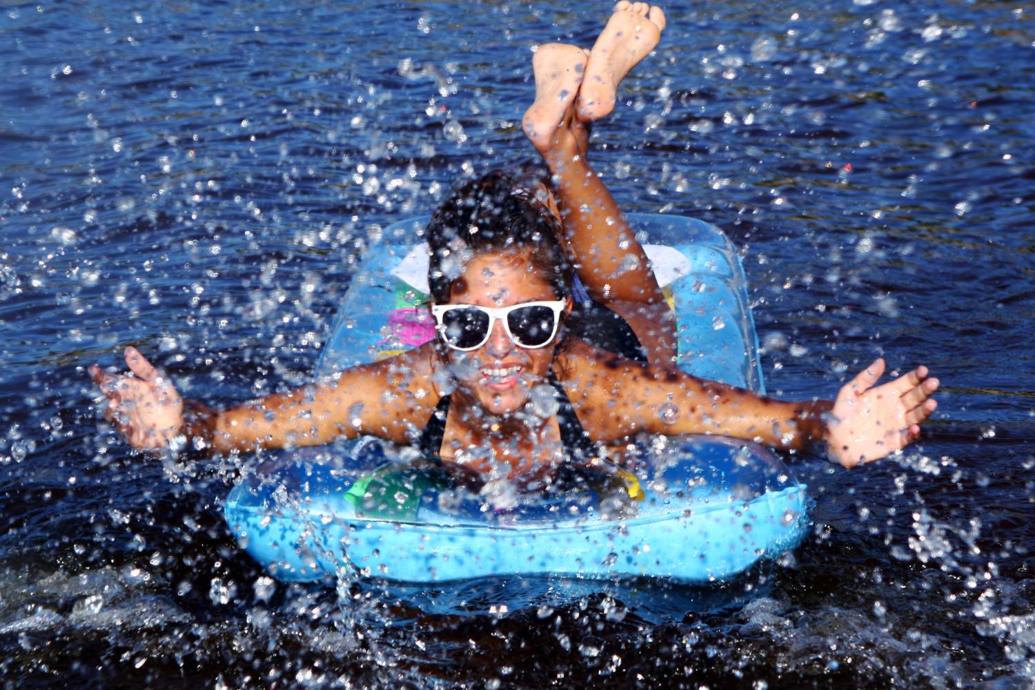 A joyful child splashing water while on a blue inflatable ring, perfect for family pontoon rentals.
