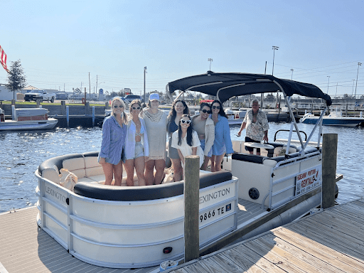A group of people smiling on a dock next to an 11-person capacity pontoon boat named "Lexington".